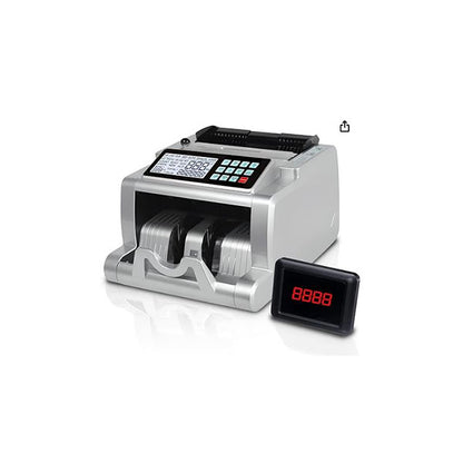 The sleek PCPOS Systems ASSUR Money Counter Machine in silver, accented with black, features an LED display and a keypad. It includes UV/MG/IR/DD counterfeit detection, counts 1000 notes/minute, and sits smartly against a white background. Ideal for office or retail use.