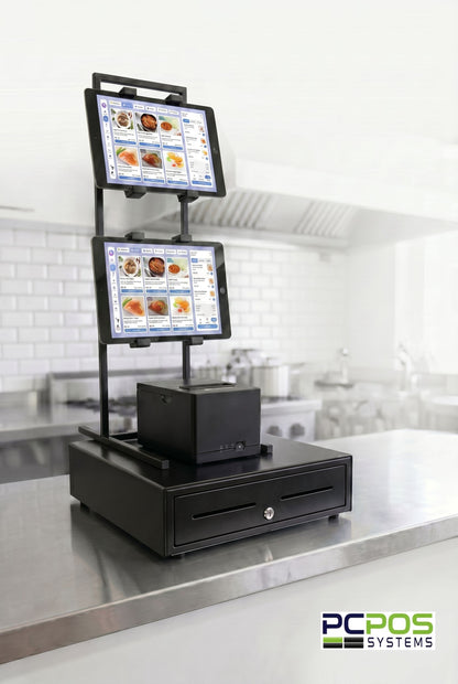 A heavy-duty PCPOS Tablet Tower by PCPOS Systems holds up to 3 tablets (7–10”) for DoorDash, Uber Eats, and POS use. It features menu displays, a receipt printer, and cash drawer, secured on a stainless steel counter in a commercial kitchen.
