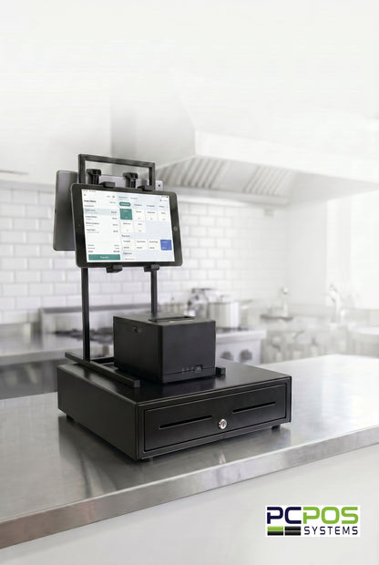 A Heavy-duty PCPOS Tablet Tower by PCPOS Systems, holding up to 3 tablets (7–10”) for DoorDash, Uber Eats, and POS, is on a stainless steel counter in a commercial kitchen with the PCPOS Systems logo in the bottom right corner.