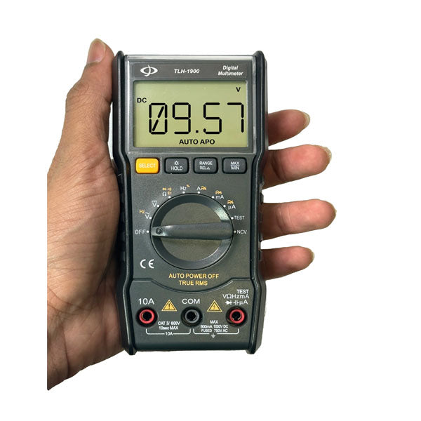A hand holding an INF digital multimeter with attached test leads. The LED display reads “09.57.” The device features a central rotary dial for selecting AC/DC voltage modes and several function buttons arranged around the screen.